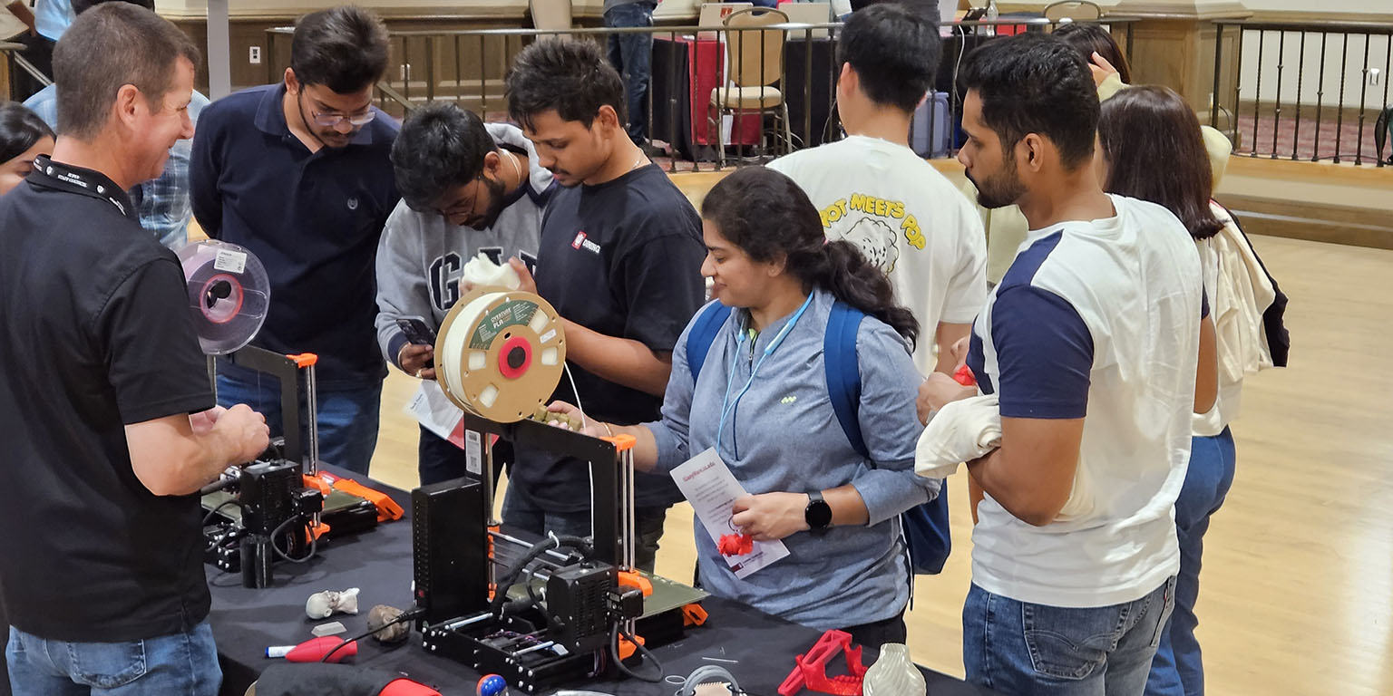 DEPI Student Outreach staffer Todd talks with students while they watch a 3D printer at tech fair 2023.