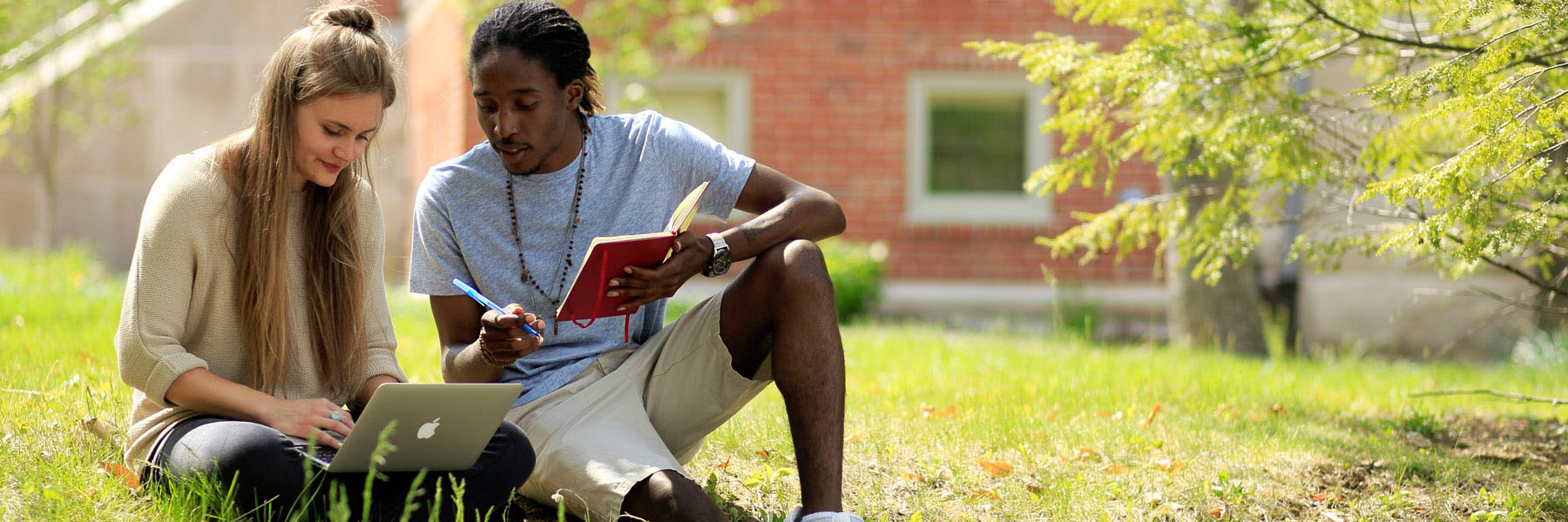 Two students sitting in the grass reading off a laptop. 